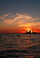 Fototapeta premium Beautiful orange sunset on sea water. Transport ship on the dock in the evening on seacoast. Shipping logistic by sea. Amazing marine landscape with colorful cloudy sky.
