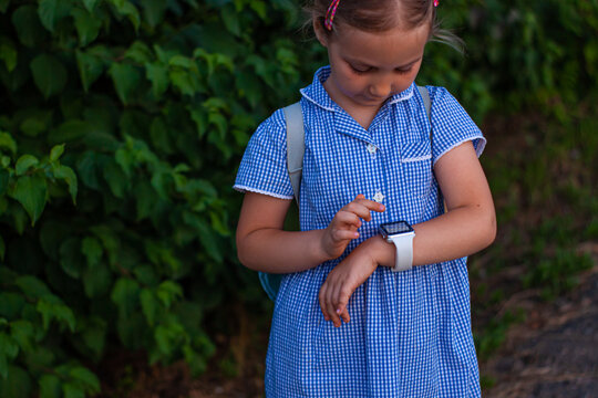 Kid using smartwatch outdoor in park. Child talking on vdeo call on the smartphone. Schoolgirl using touchscreen display on watches browsing internet. Smart wristwatch with GPS tracker.