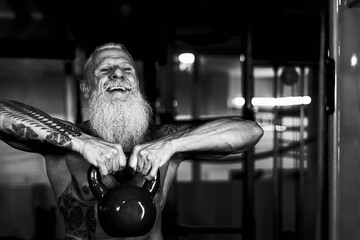 Fototapeta na wymiar Senior fitness man doing kettle bell exercises inside gym - Fit mature male training in wellness club center - Body building and sport healthy lifestyle concept - Black and white editing