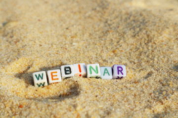 Cubes or beads labeled Webinar on a golden sandy beach with space for text