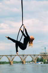 Woman aerialist performs acrobatic elements in hanging aerial hoop.