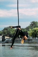Woman aerialist performs acrobatic elements in hanging aerial hoop.