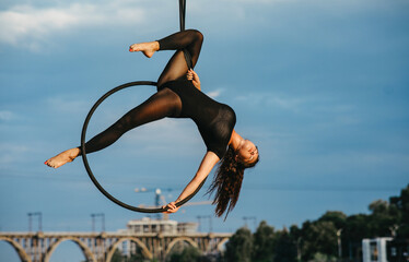 Woman aerialist performs acrobatic elements in hanging aerial hoop.