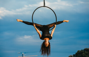 Woman aerialist performs acrobatic element split in hanging aerial hoop.