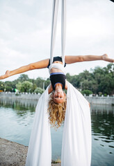 Child girl aerialist performs gymnastic split on hanging aerial silk .