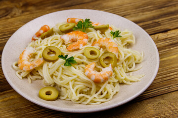 Spaghetti pasta with prawns, green olives and parsley on wooden table