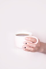 Female hands holding pink cup of black tea on pink background. Natural manicure with triangles pattern