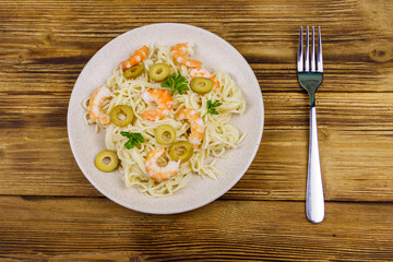 Spaghetti pasta with prawns, green olives and parsley on wooden table. Top view