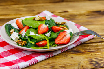 Fresh healthy salad with strawberry, spinach, walnuts and feta cheese on wooden table
