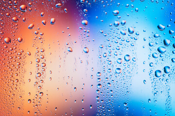 Water particles stagnant on the glass with two opposite reddish-blue colors. Blurred colorful background of droplets