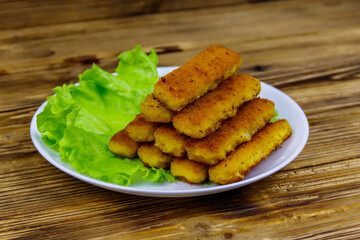 Fried fish fingers on a plate with lettuce on wooden table