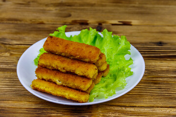 Fried fish fingers on a plate with lettuce on wooden table