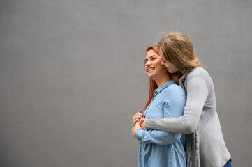 Two happy women hugging against the background of a gray wall. Gentle hugs of a female lesbian couple. LGBT Same-sex marriage.