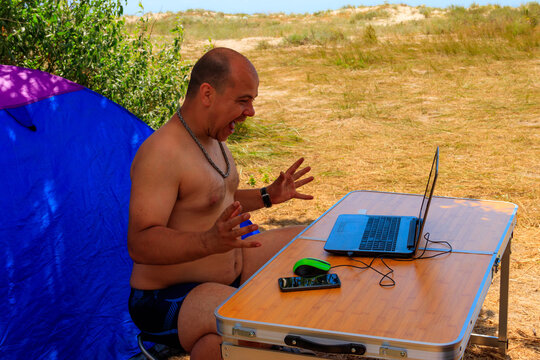 Man Using His Laptop Sitting At A Folding Picnic Table In A Camping. Working While Traveling. Freelance Work. Work And Travel Concept