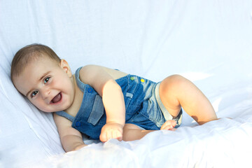 Cute Smiling baby boy with blue onesie in white sunny bedroom. children, people, infancy and age concept. Happy child