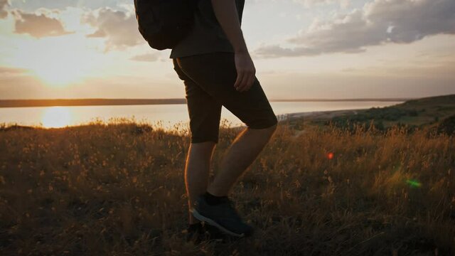 Male photographer with backpack and tripod in it is walking along meadow on plato of a mountain and enjoying view on a river. Sunrise, slow motion