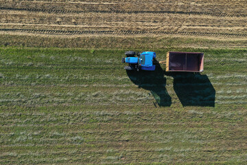 Fototapeta na wymiar A tractor transports the ripe golden wheat to the grain field harvested by the combine. Agricultural work in summer. Drone recording. Úri, Hungary - 22/07/2020