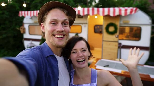 Young man and woman recording video for friends using smartphone or camera. Happy smiling couple in love showing the trailer they live in or spending vacation