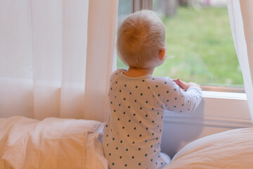 Adorable baby boy looking through the window. Stay home concept.