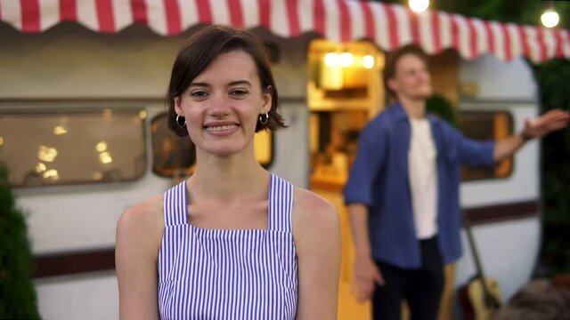 Happy cheerful couple - portrait of a pretty, brunette girl smiling at foreground and a man having fun time, dancing funny on doorstep house on wheels outdoors. Blurred background. Retro style