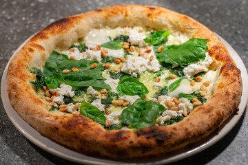 Vegetarian spinach pizza with ricotta cheese and pine nuts on a stone background.