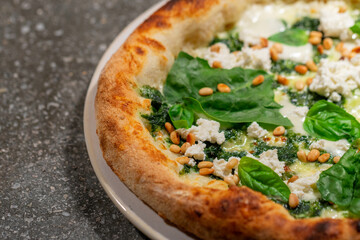 Vegetarian spinach pizza with ricotta cheese and pine nuts on a stone background.