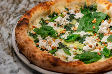 Vegetarian spinach pizza with ricotta cheese and pine nuts on a stone background.