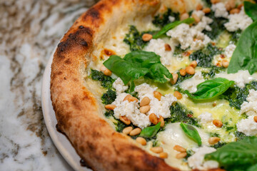 Vegetarian spinach pizza with ricotta cheese and pine nuts on a stone background.