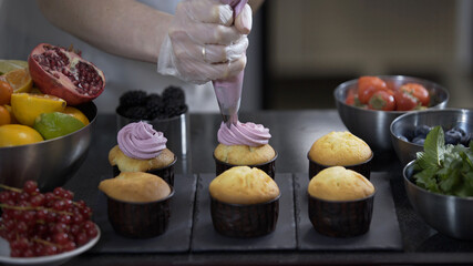 Decorating cup cake with cream. Using cooking bag, confectioner making muffins. Modern desserts and cakes. Cupcakes with cream filling. Professional pastry.