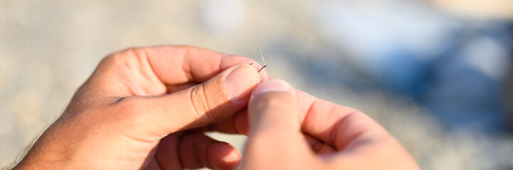 men's hands tying a fishing line on a fishing hook. selective focus. step 2. banner