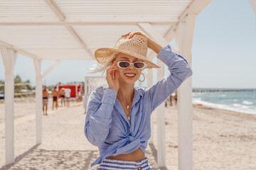 Outdoor summer fashion portrait of happy smiling woman wearing stylish straw hat, sunglasses, chain...