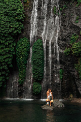 Fototapeta na wymiar A couple in love on a waterfall. Honeymoon trip. Happy couple on the island of Bali. Beautiful couple travels the world. Travel to Indonesia. Happy couple on vacation. Wedding trip. Copy space