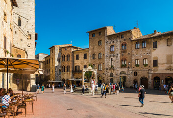 Lovely view of the popular Piazza della Cisterna, the main square of San Gimignano, Tuscany, Italy. Surrounded by medieval houses, the cistern is capped by a travertine octagonal pedestal.