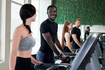 african man and caucasian female talk during sport exercises in gym. young people enjoy time in...