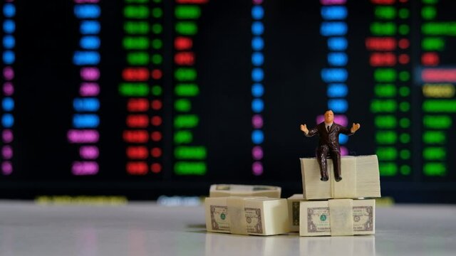 Miniature figure business people or Stock Trader sitting on Dollar Banknotes with at Blur Price Stock Ticker board on background for Graph Analysis
