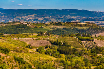 Fototapeta na wymiar Stunning view across the agricultural valleys in the countryside of the medieval hill town San Gimignano. A typical landscape with houses, olive tree orchards and vineyards on a sunny day in Tuscany.