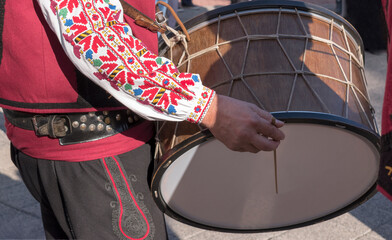 Man in Bulgarian national, traditional costume plays folk ethnic drum - tupan during wine festival...
