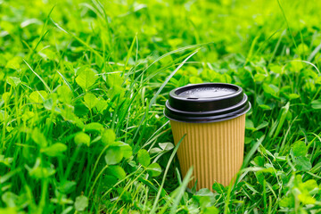 Hot paper Craft cup of coffee on the grass on a morning. Take away or delivery concept. Copy space. Summer lifestyle. Place for your text or logo on mug, mockup