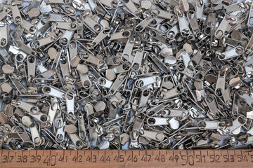 Metal slider zipper.  Group of items of metal parts for insertion into the sewing industry and a wooden measuring ruler