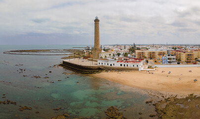 An aerial view with the drone of the big lighthouse of Chipiona on the Atlantic Ocean in western Spain. It's a cloudy summer day. In the foreground is a beach. © wewi-creative