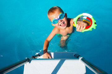 Cute  kid in goggles playing with bright rubber toys in swimming pool