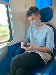 a young man travelling on a train respecting the COVID 19 measures and using a mobile phone