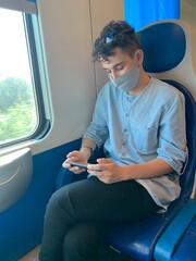 a young man travelling on a train respecting the COVID 19 measures and using a mobile phone