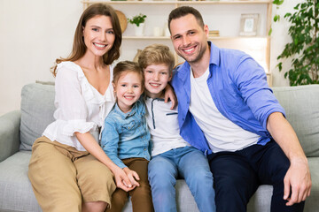 Family Hugging Sitting Together On Couch Smiling To Camera Indoor