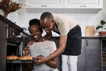 young married african couple is cooking, baking together. they are happy that everything turns out, use oven