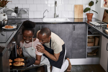 young married african couple is cooking, baking together. they are happy that everything turns out, use oven