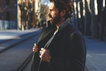 Portrait of fashionable well dressed man with beard posing outdoors looking away, confident and...