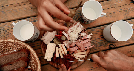 The hands of a group of people cheer with Brettljause and cups of alps milk on wooden table