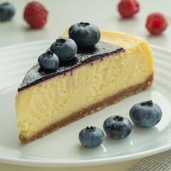 Blueberry and raspberry cheesecake, served on a white plate. Glass of milk in the sun on a white background.