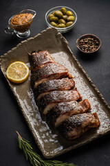 Baked carp with greens, lemon, olives and spices on a clay plate on a black background
